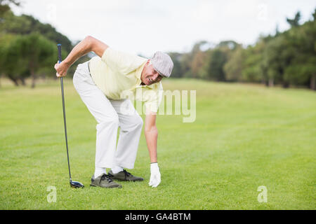 Smiling young man holding golf club et si on grassy field Banque D'Images