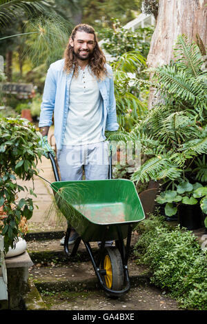 Portrait of happy gardener pushing wheelbarrow at garden Banque D'Images