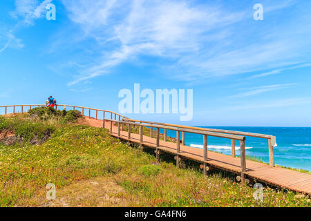 Couple de touristes debout sur la passerelle de Praia do Amado beach et à la recherche en mer, région de l'Algarve, Portugal Banque D'Images