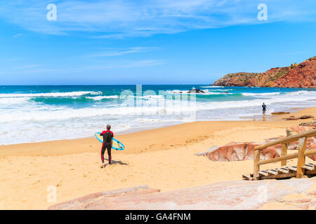 Surfer debout sur la plage Praia do Amado plage avec des vagues de l'océan de frapper la côte, région de l'Algarve, Portugal Banque D'Images