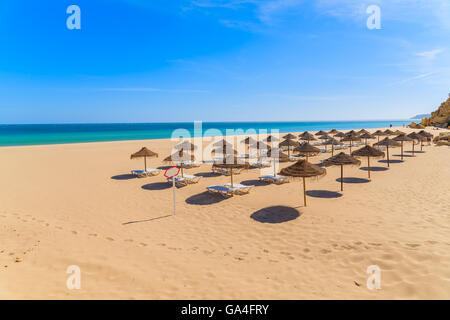 Des chaises longues avec parasols sur la plage de sable fin dans la ville balnéaire de Salema, Alrgarve région, Portugal Banque D'Images