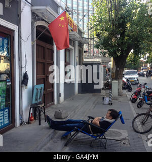 Man sleeping in street, sous un drapeau chinois Shitou, quartier de Hutong, à Pékin, en Chine. Banque D'Images