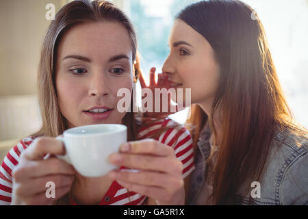 Woman whispering to friend at cafe Banque D'Images