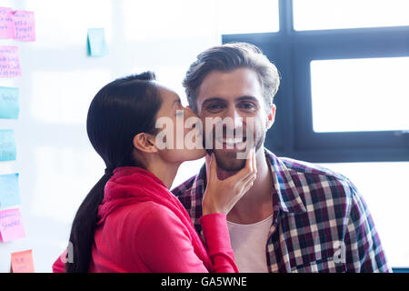 Woman kissing collègue masculin in office Banque D'Images