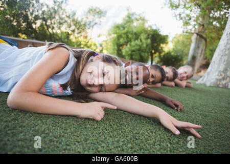 Smiling schoolkids lying on grass in campus Banque D'Images