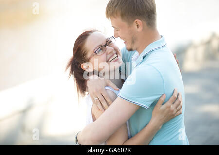 Portrait de jeune femme brune debout dans les bras de son mari en riant à l'extérieur. Ils sont à pied dans le parc sur une belle Banque D'Images