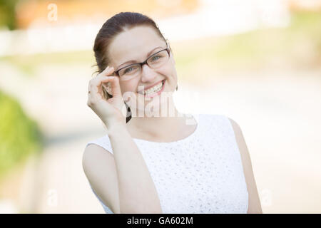 Portrait de jeune femme portant des lunettes en souriant joyeusement à l'extérieur à la caméra à l'arrière-plan lumineux contre street Banque D'Images