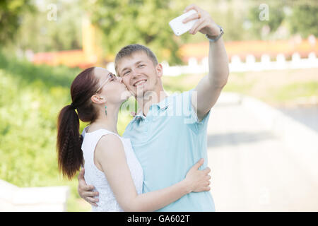 Belle jeune couple aimant debout dans Faire place au parc. Jolie femme l'embrassant bel homme. Il est tenant une Banque D'Images