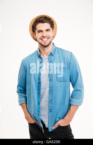 Cheerful attractive young man in hat standing with hands in pockets sur fond blanc Banque D'Images