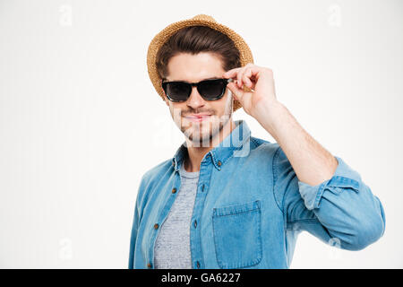 Confiant attrayante jeune homme portant chapeau et des lunettes de soleil sur fond blanc Banque D'Images