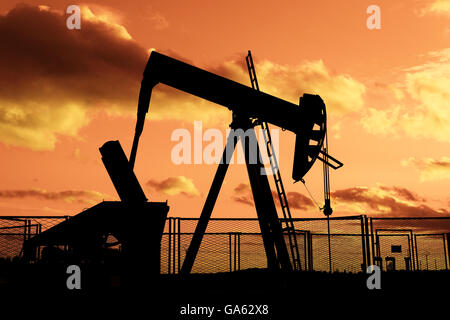 Pompage de pétrole sur fond de ciel nuageux au crépuscule Banque D'Images