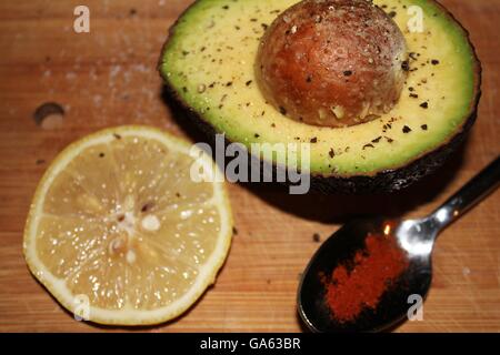 L'avocat, en pierre, assaisonnés de sel et poivre, tranche de citron et d'une cuillerée de poivre de cayenne à côte sur planche de bois. Banque D'Images