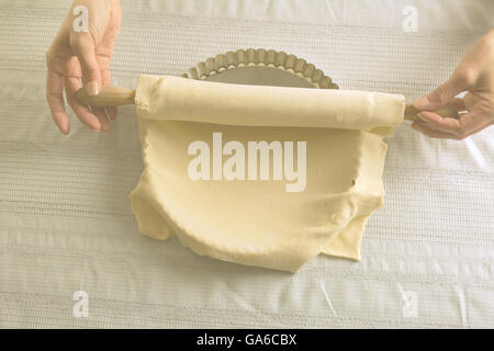 Femme plaçant stretched pâte crue avec un rouleau à pâtisserie sur une plaque de cuisson de la quiche Banque D'Images