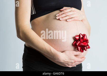 Une femme enceinte son cradels avec bow cadeau bébé ventre attaché. Banque D'Images