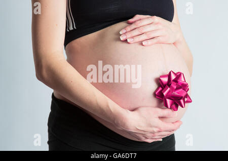 Une femme enceinte son cradels avec bow cadeau bébé ventre attaché. Banque D'Images