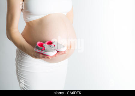 Une femme enceinte est titulaire d'une paire de chaussures de bébé en face de son ventre enceinte. Banque D'Images