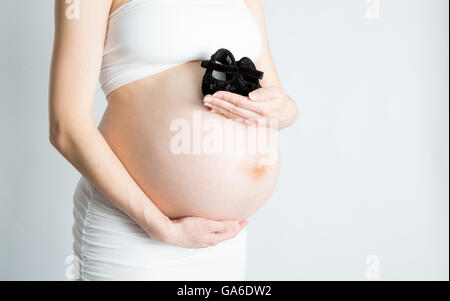 Une femme enceinte est titulaire d'une paire de chaussures de bébé en face de son ventre enceinte. Banque D'Images