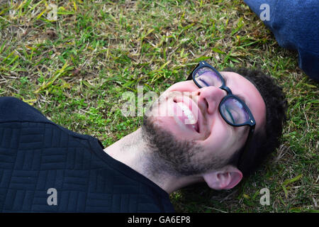 Gros plan du jeune homme latin détente sur l'herbe. Homme heureux reposant à l'extérieur. Banque D'Images