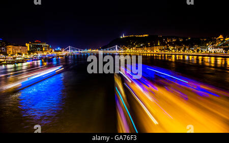 Bateaux de croisière Danube passant sous le pont des Chaînes nuit Budapest Hongrie. Elizabeth Bridge dans la distance Banque D'Images