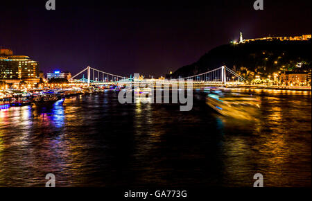 Bateaux de croisière Danube passant sous le pont des Chaînes nuit Budapest Hongrie. Elizabeth Bridge dans la distance Banque D'Images