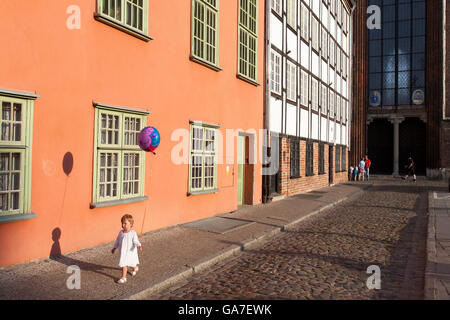 Une petite fille marche tenant un ballon, en passant devant un bâtiment coloré, son ombre marcher avec elle à Gdansk, Pologne Banque D'Images