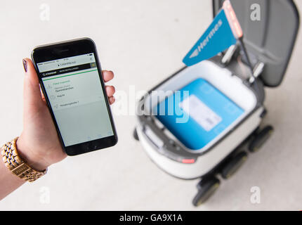 ILLUSTRATION - une femme peut contenir jusqu'son smartphone avec une confirmation de livraison avant d'un robot développé par la société Starship Technologies pour la livraison de colis Hermes, qui est porteur d'une parcelle, à Hambourg, Allemagne, 04 août 2016. En août Hermes a commencé un test-run de la livraison du robot à Hambourg. Photo : DANIEL BOCKWOLDT/dpa Banque D'Images