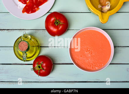 Capture d'un grand angle d'un bol avec de l'espagnol et gaspacho ingrédients certains de les préparer, comme la tomate, l'ail et l'huile d'olive, sur un bl Banque D'Images