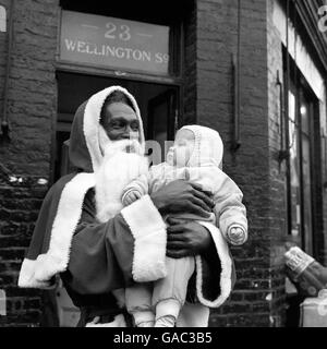 Joe Cole, qui est venu en Grande-Bretagne du Nigeria il y a vingt ans, est Père Noël à la boutique de Philip Townsend à Little Clarendon Street, Oxford. Santa Joe, vu avec Jeremy Taylor, neuf mois, a obtenu le poste parce qu'il était la personne la plus heureuse et la plus joviale que M. Townsend puisse trouver. Banque D'Images