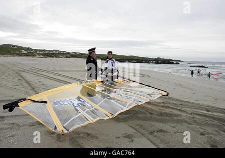 Le policier local Danny Lapsley de la police de Strathclyde, qui est le seul officier sur l'île de Tiree, parle avec le windsurfeur finlandais Tuomo Naalisvaara pendant son battement sur la plage de Balevullin sur l'île de Tiree. Banque D'Images