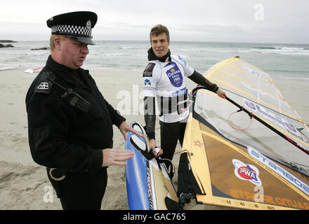 Le policier local Danny Lapsley de la police de Strathclyde, qui est le seul officier sur l'île de Tiree, parle avec le windsurfeur finlandais Tuomo Naalisvaara pendant son battement sur la plage de Balevullin sur l'île de Tiree. Banque D'Images