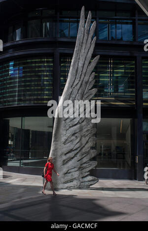 Les travailleurs de la ville par le passage de l'oeuvre d'un géant de l'aile de bronze lors d'un midi de printemps dans le quartier financier de Londres, le 4 juillet, Londres, Royaume-Uni. Comme la lumière se reflète sur les immeubles de bureaux à proximité, la foule à l'heure du déjeuner devant ce géant des illustrations sur leur façon de réunions et sandwicheries. Les dix mètres de haut est la sculpture en bronze par le président de la Royal Academy of Arts, Christopher Le Brun, commandé par Hammerson en 2009. Elle est appelée 'La Ville' de l'aile et a été jeté par Morris Singer, fondateurs de l'art réputé pour être la plus ancienne fonderie d'art dans le monde. Banque D'Images