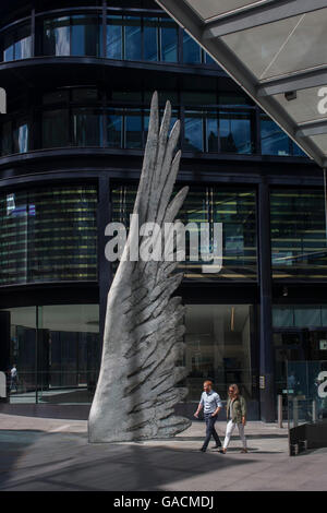 Les travailleurs de la ville par le passage de l'oeuvre d'un géant de l'aile de bronze lors d'un midi de printemps dans le quartier financier de Londres, le 4 juillet, Londres, Royaume-Uni. Comme la lumière se reflète sur les immeubles de bureaux à proximité, la foule à l'heure du déjeuner devant ce géant des illustrations sur leur façon de réunions et sandwicheries. Les dix mètres de haut est la sculpture en bronze par le président de la Royal Academy of Arts, Christopher Le Brun, commandé par Hammerson en 2009. Elle est appelée 'La Ville' de l'aile et a été jeté par Morris Singer, fondateurs de l'art réputé pour être la plus ancienne fonderie d'art dans le monde. Banque D'Images