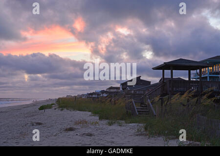 Les nuages de tempête au coucher du soleil sur la plage des chalets sur l'Atlantique sur la plage de Long Beach, à Oak Island Caroline du Nord. Banque D'Images