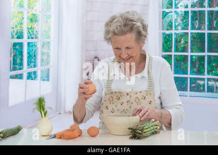 Femme âgée dans le bol les oeufs de fissuration dans la cuisine Banque D'Images