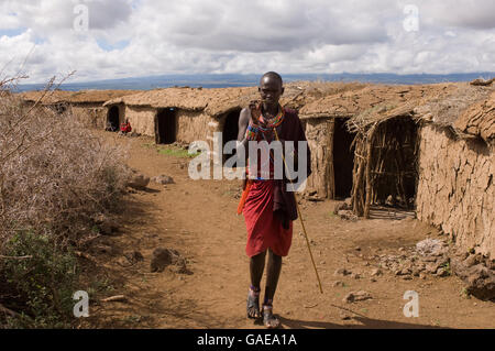 Le Masai homme debout en face de cabanes, Parc National d'Amboseli, Kenya, Africa Banque D'Images