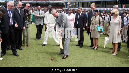 Le Prince de Galles (au centre) essaie sa main avec une batte de cricket lors d'une visite à l'ovale du parc de la Reine dans la capitale de Trinité-et-Tobago, Port of Spain, comme le regarde la duchesse de Cornouailles (à droite). Banque D'Images