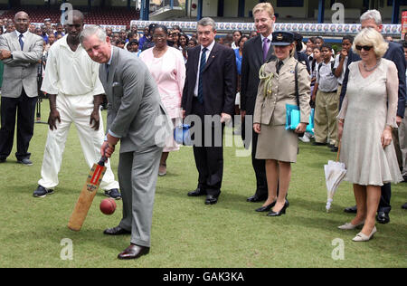 Le Prince de Galles (au centre) essaie sa main avec une batte de cricket lors d'une visite à l'ovale du parc de la Reine dans la capitale de Trinité-et-Tobago, Port of Spain, comme le regarde la duchesse de Cornouailles (à droite). Banque D'Images