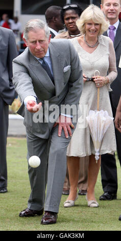 Le prince de Galles essaie sa main avec une balle de cricket lors d'une visite à l'ovale du parc de la Reine dans la capitale de la Trinité-et-Tobago, Port of Spain, comme le regarde la duchesse de Cornwall. Banque D'Images