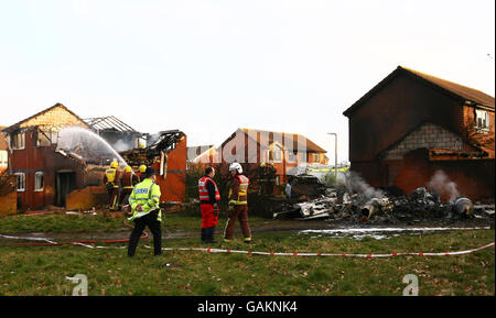 Un pompier serra aujourd'hui une maison à Broadwater Gardens Farnborough, dans le Kent, où un avion privé a heurté la propriété.L'épave de l'avion peut être vue à droite. Banque D'Images