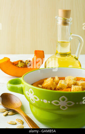 Soupe au potiron avec des croûtons et graines de citrouille dans un bol vert sur fond de bois blanc, vertical Banque D'Images