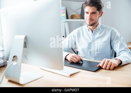 Heureux jeune homme designer, à l'aide d'ordinateur et tablette graphique sur le lieu de travail Banque D'Images