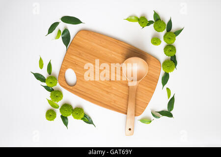 Planche à découper en bois et louche à décor de fleurs de chrysanthèmes et de ficus feuilles sur fond blanc. Vue de dessus. Fla Banque D'Images