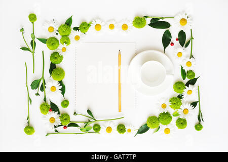 Papier, crayon et une tasse de café ou de thé avec floral frame à partir de camomille et de fleurs de chrysanthème, ficus feuilles et ripe rowan Banque D'Images