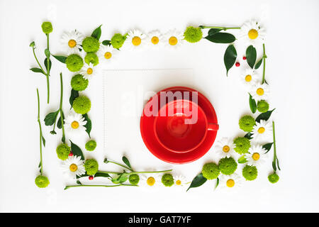 Tasse rouge et du papier pour le café ou le thé avec floral frame à partir de camomille et de fleurs de chrysanthème, ficus feuilles et ripe rowan sur w Banque D'Images