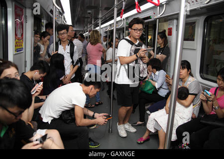 La circonscription du peuple chinois Guangzhou Metro train, certains assis d'un certain rang, certains jouant avec leurs smartphones. Guangzhou. Banque D'Images