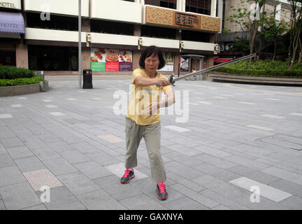 Une vieille femme chinoise à la retraite est très intense et se concentrer comme elle le fait le Tai Chi dans un parc public à l'aide d'une lance. Kowloon, Hong Kong. Banque D'Images