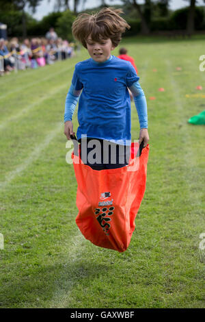 Garçon concurrentes dans race sac de sport à l'école primaire St James à Chipping Campden jour uk Banque D'Images