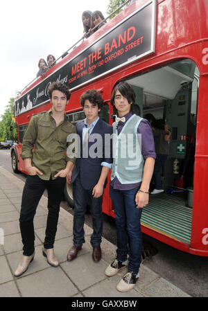 (De gauche à droite) Kevin, Nick et Joe Jonas des Jonas Brothers posent à côté d'un bus à toit ouvert dans le centre de Londres. Banque D'Images