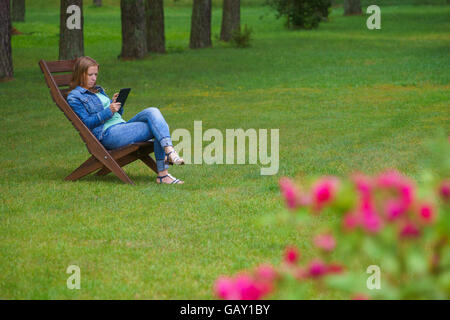 Jeune femme sérieuse travaillant sur un tablet PC dans le jardin en été. Banque D'Images