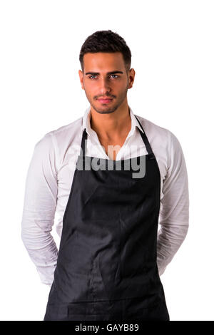 Jeune cuisinier ou serveur posant, accueille ses hôtes avec un sourire, le port de tablier noir et chemise blanche isolé sur fond blanc Banque D'Images